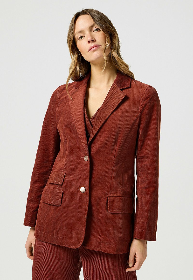 Roestkleurig corduroy blazer met een geknopt revers, twee voorzakken en zilveren knopen. Beschikt over een verticale ribbelstructuur en een getailleerde pasvorm.