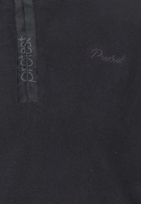 Gros plan d'un tissu polaire noir avec une fermeture éclair verticale et le logo "Protest" imprimé et brodé sur la zone de la poitrine.