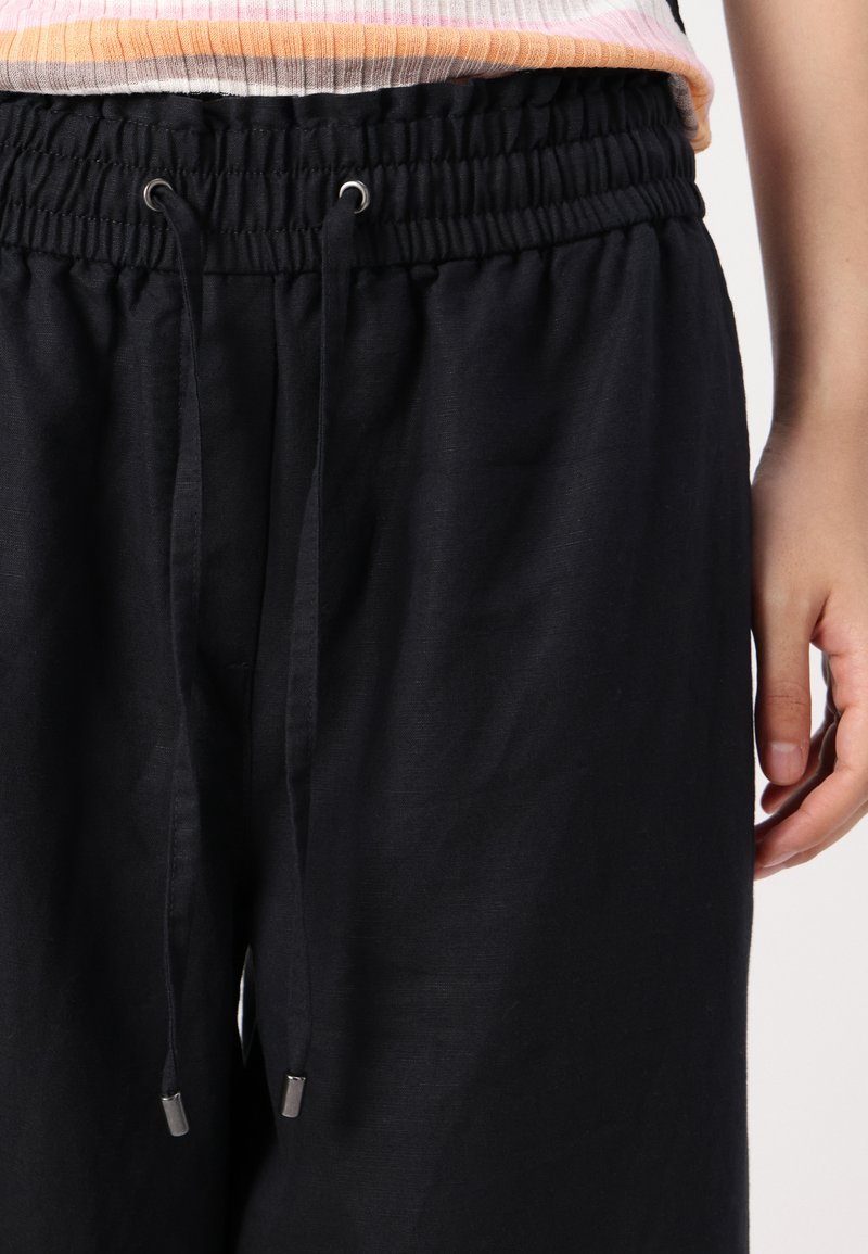 Schwarze Jogginghose mit elastischem Bund, Kordelzugverschluss und Metallspitzen. Das Material wirkt leicht und hat eine leicht strukturierte Oberfläche.