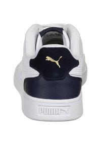 Białe tenisówki z granatowym zamszowym piętem, skórzanymi akcentami o fakturze oraz złotym logo Pumy na pięcie. Czysty, sportowy design.