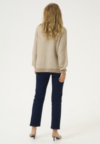 Beige stickad tröja med mönstrad textur, ribbade ärmslut och nederkant, tillsammans med mörkblå slim fit-jeans och svarta sandaler.