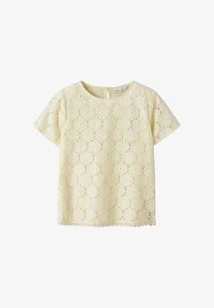 Krem bluzica s kratkimi rokavi iz čipke z rožnim vzorcem, okrogel izrez in zapenjanje na gumbe na zadnji strani, primerna za vsakodnevne ali bolj svečane priložnosti.