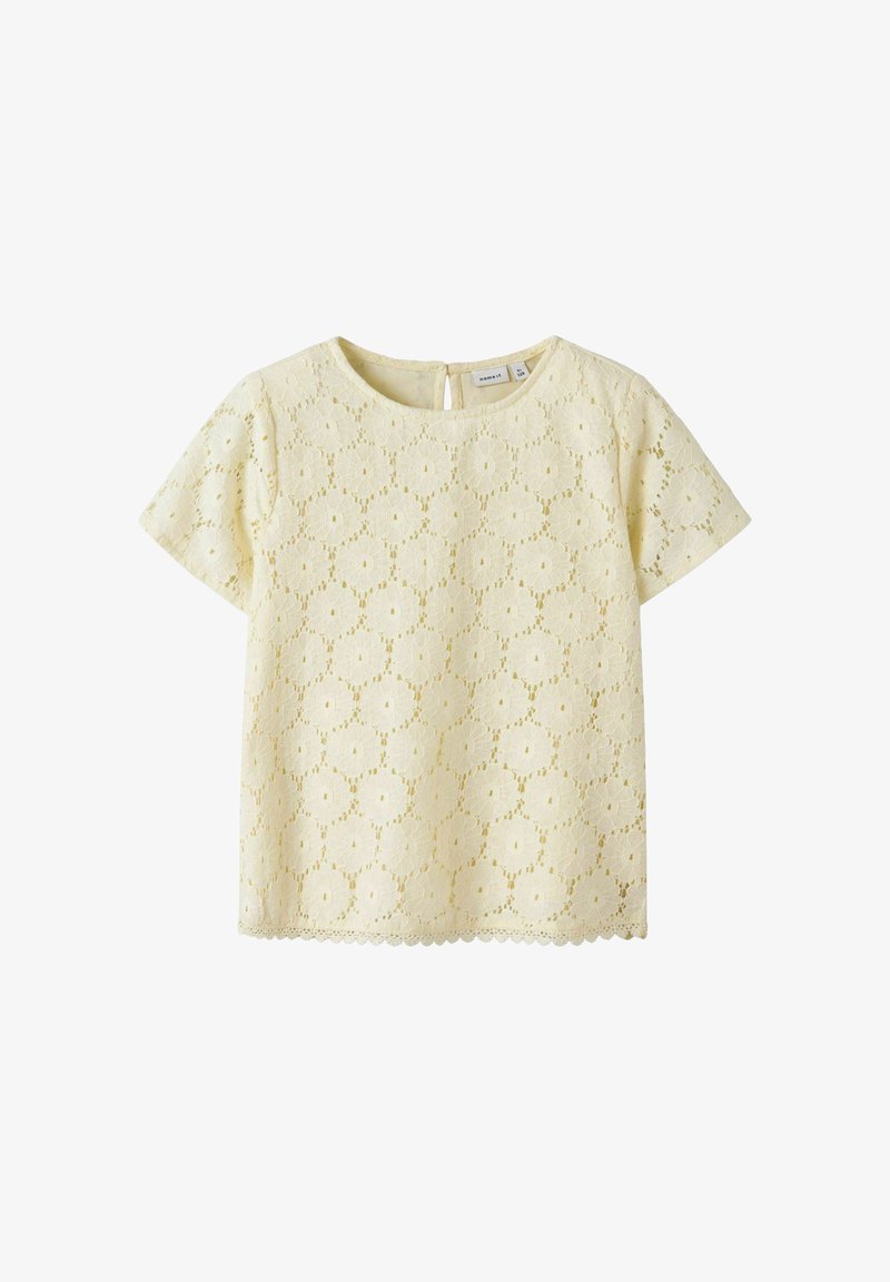 Kremowa bluzka z krótkim rękawem z kwiatowym wzorem z koronki, okrągłym dekoltem i zapięciem na guziki z tyłu, odpowiednia na okazje codzienne i bardziej eleganckie.