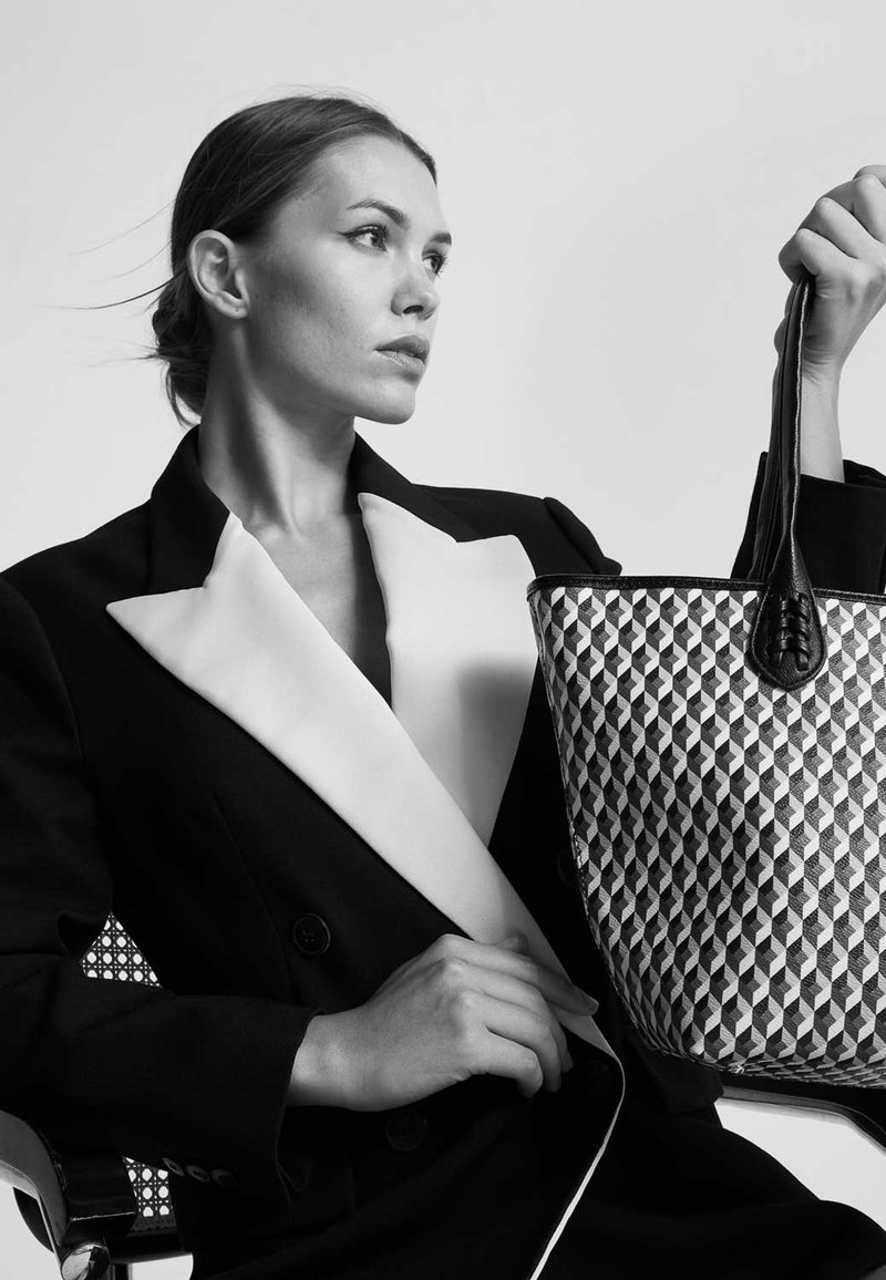 Borsa a tracolla geometrica in bianco e nero con dettagli in pelle nera, tenuta da una persona che indossa un blazer strutturato nero con un colletto crema.