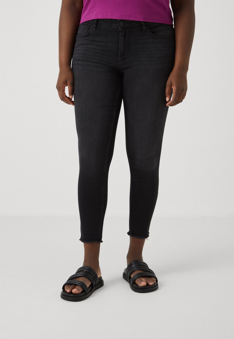 Black skinny jeans with a high waist, distressed hem, and a smooth texture, paired with black multiple strap sandals.