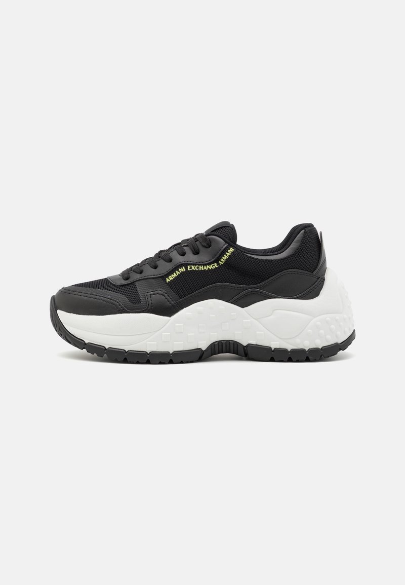 Baskets épaisses noires et blanches avec semelle texturée épaisse, lacets noirs, empiècements en mesh et logo jaune Armani Exchange sur le côté.