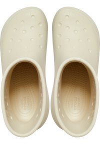 Sabots beige clair avec un extérieur lisse, percés de petits trous ronds. L'intérieur présente des motifs texturés pour une meilleure adhérence et un confort optimal.