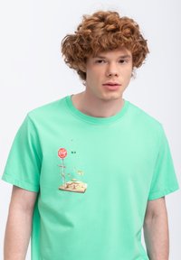 T-shirt in cotone verde chiaro con stampa grafica di un cartello di stop e elementi artistici, dalla vestibilità rilassata e con scollatura rotonda.