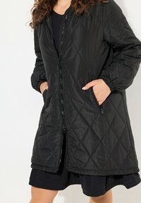 Cappotto trapuntato nero con polsini elasticizzati e due tasche laterali. Presenta una chiusura con zip completa e un orlo leggermente svasato per una vestibilità comoda.