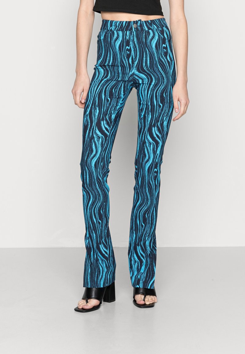 Blå mönstrade byxor med ett vågigt mönster på en mörk bakgrund, parat med svarta blockklack-sandaler. Slim fit och mid-rise midja.