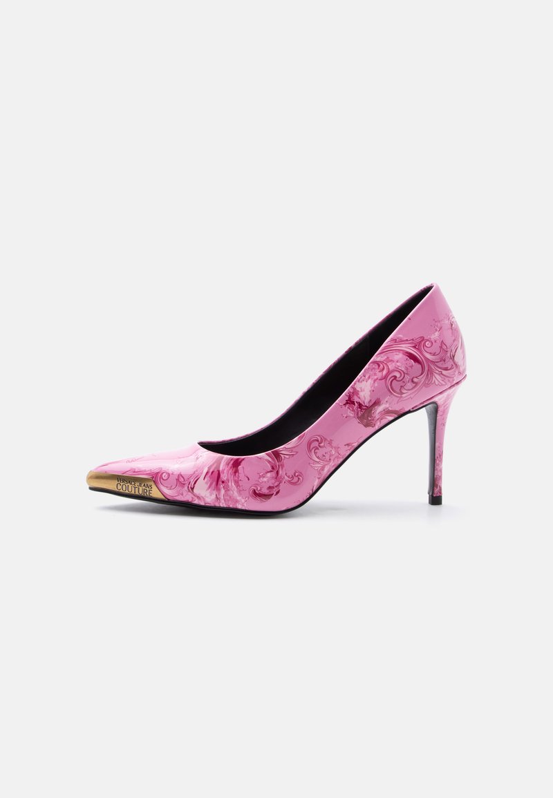 Ροζ γυναικείες γόβες με ψηλό τακούνι, διακοσμημένες με φλοράλ μπαρόκ σχέδιο και χρυσή λεπτομέρεια στη μύτη, χαραγμένη με τη φράση "Versace Jeans Couture" σε λευκό φόντο.