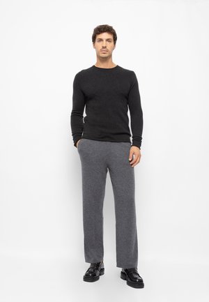 Γκρι παντελόνι από μείγμα μαλλιού και μαύρο πουλόβερ με μακριά μανίκια, φορεμένα με γυαλιστερά μαύρα παπούτσια, τοποθετημένα σε λευκό φόντο.