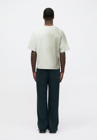 Ανοιχτό γκρι κοντομάνικο μπλουζάκι με χαλαρή εφαρμογή. Συνδυάζεται με σκούρα μπλε τζιν σε φαρδύ κόψιμο που διαθέτουν πίσω τσέπες, εμφανίζεται από το πίσω μέρος.