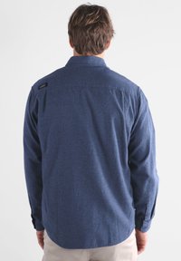 Camisa de manga larga azul oscuro, hecha de una tela texturizada, con un cuello abotonado y costuras visibles a lo largo de las costuras.