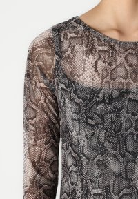 Majica z dolgimi rokavi iz prozorne tkanine z sivim in rjavim vzorcem kačjega usnja. Okrogli ovratnik, prilegan kroj in gladka tekstura.