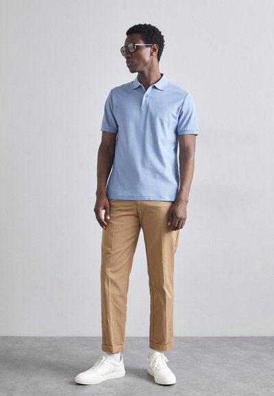 Light blue polo shirt with a collar, beige rolled-up trousers, and white sneakers. Accessories include sunglasses and earrings.