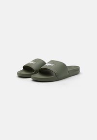 Zöld, szintetikus anyagból készült strandpapucs, nyitott orrészű, széles pánttal és hímzett logóval a felső részen.
