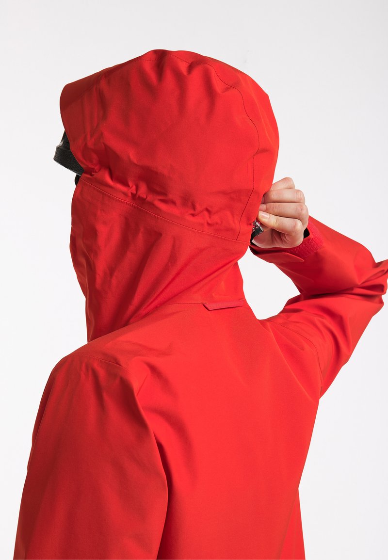 Červená nepromokavá bunda s vysokým límcem a nastavitelnou kapucí, s hladkou texturou a předním zapínáním.
