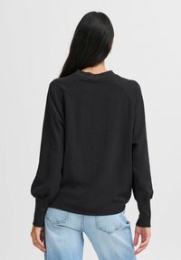 Felpa nera a maniche lunghe con un finish testurizzato e maniche raglan, abbinata a jeans azzurri chiari. Design minimalista, senza loghi visibili.