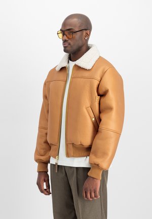 Braune Lederbomberjacke mit einem weißen Schafsfellkragen, gerippten Bündchen und Saum, goldener Reißverschluss und einer seitlichen Druckknopftasche.