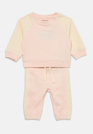 Zweiteiliger Babyanzug mit langärmligem rosa-cremefarbenem Sweatshirt mit dem Schriftzug „calvin klein“ und passenden rosa Hosen mit cremefarbenen Seitenstreifen.