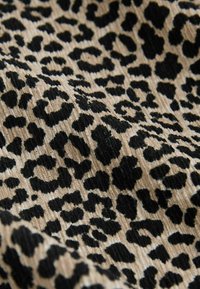 Țesătură cu imprimeu leopard pe un fundal bej și cu pete negre, având o textură cu striații. Modelul are dimensiuni și forme variate ale petelor.