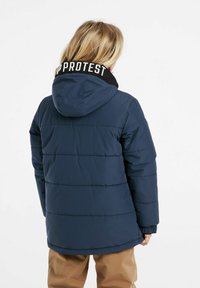 Giubbotto imbottito blu navy con cappuccio nero, con il logo bianco "PROTEST" sul colletto. Ha una finitura testurizzata e polsini elastici.