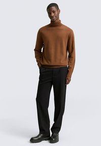 Bruine coltrui, slim-fit, gecombineerd met zwarte broek en zwarte enkellaarsjes. Gladde textuur, minimalistisch ontwerp, neutrale achtergrond.