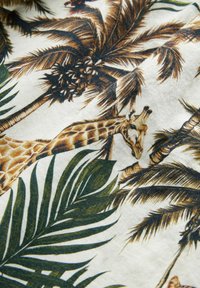 Tissu tropical mettant en scène une girafe au milieu de palmiers verts, sur un fond beige avec des illustrations détaillées et texturées.