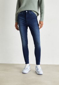 Jeans skinny de un azul oscuro con una cintura de altura media y diseño de cinco bolsillos, combinados con zapatillas de deporte azul claro con detalles en blanco.