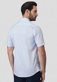 Koszula z krótkim rękawem w jasnoniebieskim kolorze z małymi granatowymi kropkami, z kołnierzykiem zapinanym na guziki, zaokrąglonym dołem oraz gładką teksturą materiału.