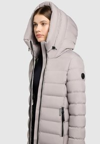 Padded light gray jacket with a large hood, zipper closures, and side pockets. Features ribbed texture and logo on the sleeve.
