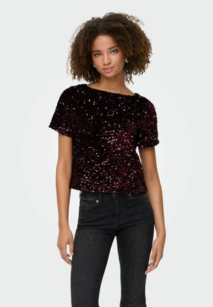 Top de lentejuelas burdeos con mangas cortas, escote redondeado y tejido texturizado. Combinado con jeans negros que presentan sutiles acentos de brillo.