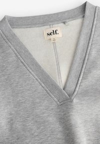 Pullover grigio con design a V, caratterizzato da bordi ribattuti e foderatura interna morbida. L'etichetta indica "self." con taglia S.