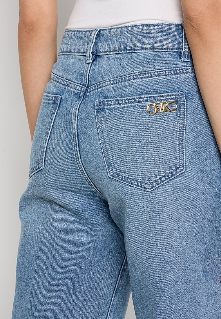 Vaqueros de mezclilla de color azul claro con cintura alta, corte recto y un acento de logo dorado en el bolsillo trasero. Se aprecian los detalles de costura estándar.