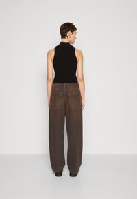 Schwarzes ärmelloses Oberteil mit hohem Kragen, kombiniert mit weiten, braunen Jeanshosen, die über Gesäßtaschen und Nähdetails verfügen.