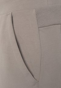 Helle graue Sweatpants mit weicher Textur, geripptem Bund und seitlicher Tasche mit sichtbaren Nähdetails.