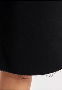 Jupe en tissu noir avec une finition texturée, ourlet brut avec bords effilochés. Design simple et droit sans motifs.