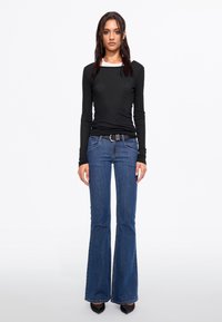 Black long-sleeve top with white neckline, paired with blue flared jeans and black heels. Simple design with fitted silhouette and classic colors.