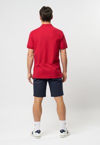 Czerwona bawełniana koszulka polo z kołnierzykiem, zestawiona z granatowymi spodniami krótkimi. Widoczne logo na butach, białe skarpetki z teksturowanym wzorem.