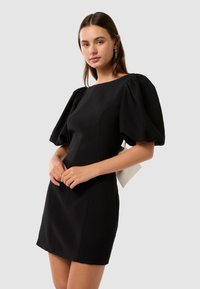 Abito nero con maniche a sbuffo, scollatura rotonda e silhouette aderente. Tessuto liscio con dettagli di cucitura sottili.