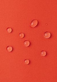 Tessuto di un vivace arancione testurizzato con diverse goccioline d'acqua chiare adagiatesi sulla superficie, che evidenziano le proprietà idrofobiche.