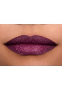 Rossetto viola opaco applicato su labbra lisce, con texture e definizione visibili, su uno sfondo di tono della pelle chiaro.