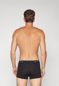 Fekete Calvin Klein boxer alsónadrág, logós derékpánttal, szoros illeszkedéssel és sima szövettextúrával, hátulról mutatva.