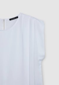 Blusa bianca a maniche corte, realizzata in tessuto morbido. Presenta pieghe verticali sul davanti e una chiusura sul retro a forma di chiave.
