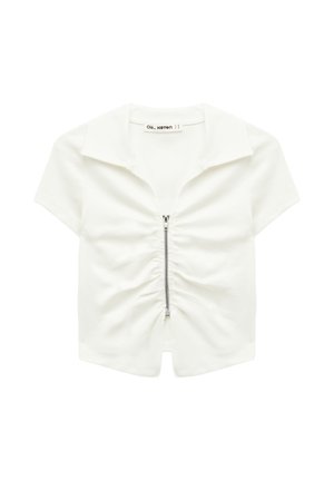 Valkoinen lyhythihainen lyhyt paita, jossa on kaulus ja etuosassa hopeanvärinen vetoketju. Vetoketjun kohdalla laskostettua kangasta.