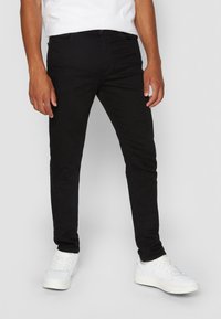Jeans ajustados negros de denim, con un diseño clásico de cinco bolsillos y detalles de costura sutiles, combinados con zapatillas blancas.