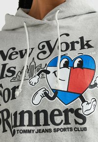 Ljusgrå hoodie med en grafisk bild av ett tecknat hjärta med blå och röda sektioner, svart text och snöre vid halsringningen.