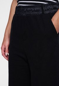 Zwarte joggingsbroek van zachte stof, met een elastische tailleband, zijzakken en een gladde textuur met subtiele stikseldetails.