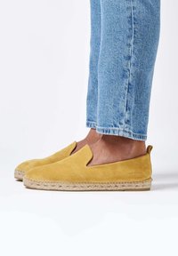 Espadrilles de ante amarillo sin cordones con suela de yute trenzada. Combinados con unos pantalones vaqueros de denim azul claro, con un corte informal y un ligero deshilachado.